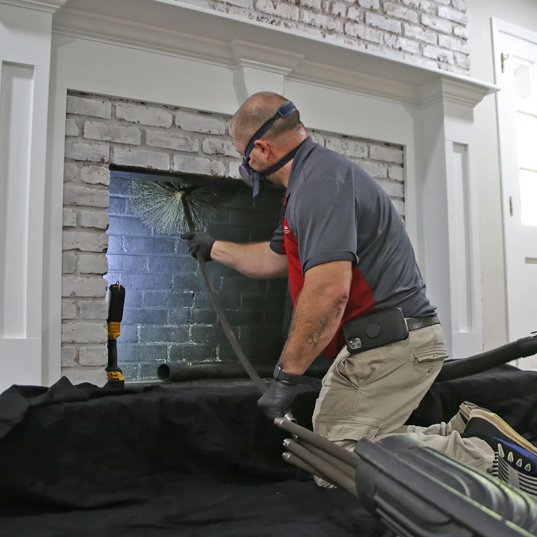Chimney technician cleaning a white-brick residential fireplace