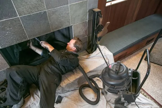 Technician cleaning a fireplace with protective coverings and vacuum equipment